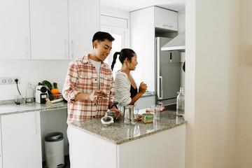 A man holds a spoon and smiles while a woman stands and talks next to him at the table