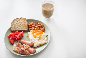 Plate with fried egg, bacon, sausages, beans, tomatoes, and toast served with a cup of coffee on a white table, symbolizing breakfast, energy, and traditional morning meal