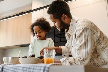 The daughter looks at the plates in which her father, who is standing next to her at the table, holds cutlery