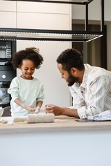 A father and his daughter stand at the table and look at her hands in flour