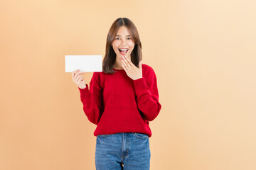 Happy Asian business woman standing and hold blank paper or gift voucher mockup on beige color background.