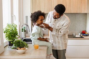 The father stands and wipes the mouth of his daughter sitting on the table with a napkin