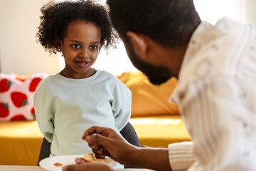 The daughter sits at the table and smiles while listening to her father