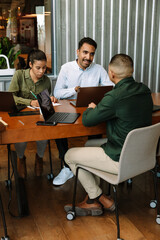 A group of three workers are sitting at a table and talking while one of them writes
