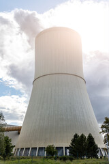 Tall cooling tower releasing steam into blue sky, symbol industrial energy production and technology. The structure represents power generation, heat emission and environmental engineering in Germany