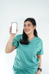 Naklejka premium Smiling female healthcare worker in green medical uniform holding a smartphone with a blank white screen, isolated on white background. Concept of telemedicine, online consultation, and digital healt