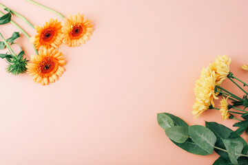 Yellow and orange flowers with green leaves on peach background. Flat lay floral arrangement with copy space