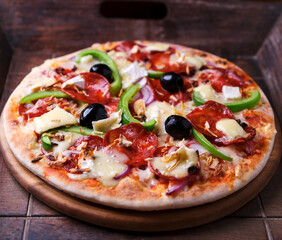 Pizza with chorizo ​​sausage, mozzarella cheese, green pepper and black olives. Rustic wooden background. Soft focus.	