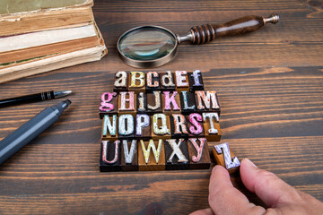 Complete alphabet made from colorful vintage wooden letterpress blocks with magnifying glass and old books on wooden desk symbolizing learning education and typography