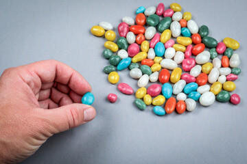 Hand picking colorful candy from pile on gray background symbolizing choice temptation and decision concept in unhealthy eating and nutrition