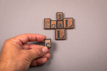 Words goal and sale made from vintage wooden letterpress blocks with human hand arranging letters on gray background symbolizing business success and marketing strategy