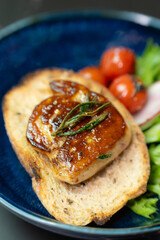 Seared French foie gras and roasted tomatoes on crunchy toast, garnished with fresh greens, are elegantly presented on a unique blue stone plate for a gourmet starter