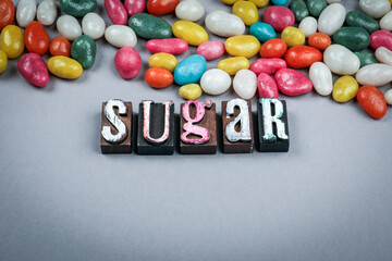 Word sugar made from vintage wooden letterpress blocks with colorful candies on gray background symbolizing sweetness energy and unhealthy nutrition concept