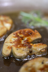 Sizzling pan-seared foie gras with fresh thyme sprigs in a hot skillet, creating a rich, aromatic French gourmet delicacy