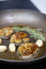 Delicious seared foie gras with fresh thyme sprigs and aromatic garlic cloves sizzling in a hot pan, highlighting the gourmet French cooking process