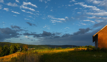 Abendliches Sonnenlicht mit Wolken über Feld und Wald auf dem Dorf