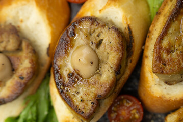 Delicious seared foie gras on toasted bread, garnished with savory roasted vegetables, including tomatoes, and aromatic garlic