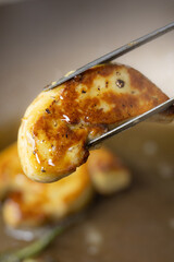 Chef's Tongs Lifting a Perfectly Seared, Golden-Crusted Foie Gras Slice from the Hot Pan, Highlighting Rich, Decadent Juiciness © M Stocker