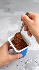 Hands holding a small container of instant coffee granules