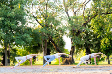 Four women perform a synchronized dynamic yoga flow pose outdoors, demonstrating strength, focus, and perfect alignment in a natural park setting.