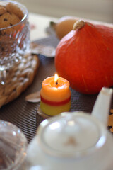 Lit candles, cookies, chocolate, nuts, tea, wine, pumpkins, books, reading glasses and autumn leaves on the table. Autumnal hygge at home. Selective focus.