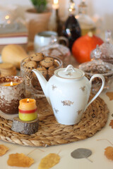 Lit candles, cookies, chocolate, nuts, tea, wine, pumpkins, books, reading glasses and autumn leaves on the table. Autumnal hygge at home. Selective focus.