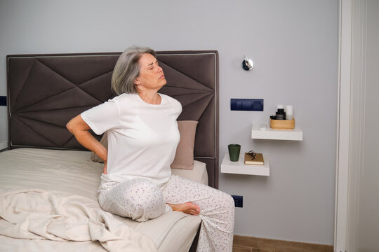 Person with back pain sitting on bed in bedroom in the morning