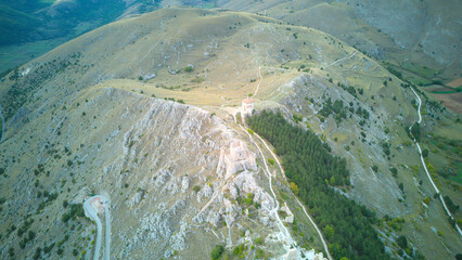 Drone aerial view of Monte Calascio, Abruzzo, featuring the medieval Rocca fortress and spectacular surrounding mountain landscapes