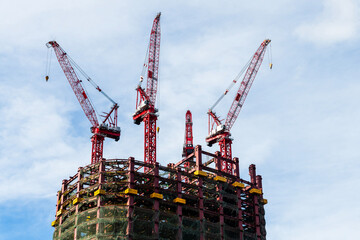 Low-angle view of cranes and steel structures of building construction with a blue sky background in Taiwan.