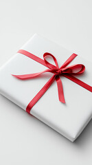 White gift box with red satin ribbon on white background, minimal holiday or romantic present.
