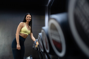 Portrait of smiling caucasian fitness woman standing by dumbbell weights preparing for...