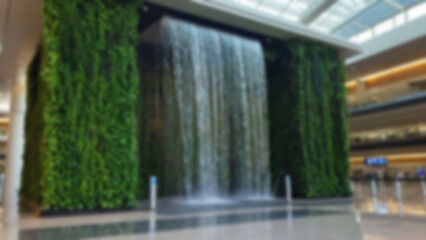 Blurred background of an artificial waterfall located in the middle of the airport with vines in a modern and environmentally friendly airport.
