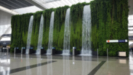 Blurred background of an artificial waterfall located in the middle of the airport with vines in a modern and environmentally friendly airport.