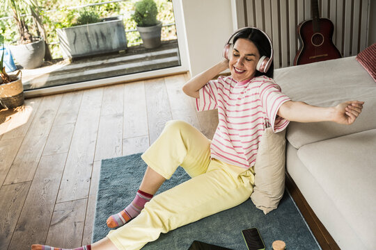 Cheerful woman listening to music through wireless headphones sitting at home