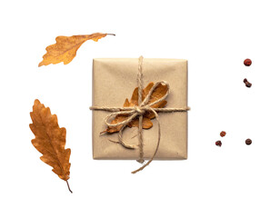A square wrapped present, tied with twine and a dried leaf, resting with leaves and peppercorns