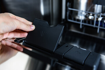 Woman putting detergent capsule into dishwasher.