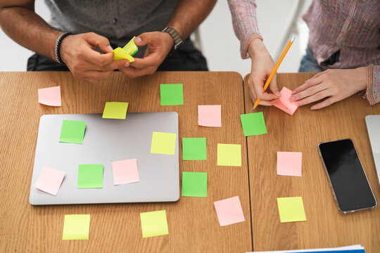 Two people collaborate at a wooden desk, using sticky notes and a laptop for brainstorming and planning.