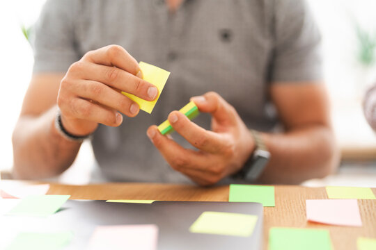 A person is holding and arranging colorful sticky notes on a desk, symbolizing planning and organization.