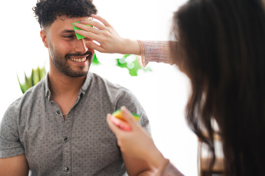 A woman places a green sticky note on a smiling man's forehead as they play a guessing game together.