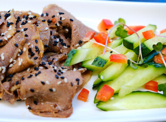 Close up of sliced boiled beef tongue arranged with cucumbers and bell peppers sprinkled with sesame seeds microgreens and garlic seasoned with olive oil and soy sauce for elegant homemade serving.