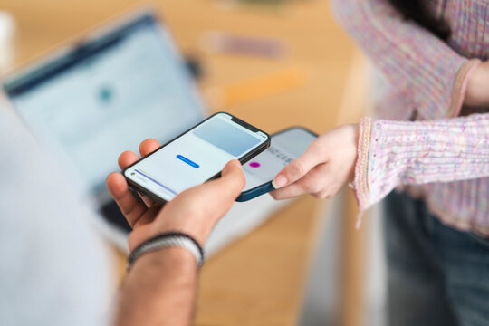 A person holds a smartphone displaying a payment interface, while another person's hand reaches out to tap their own device for a contactless transaction.