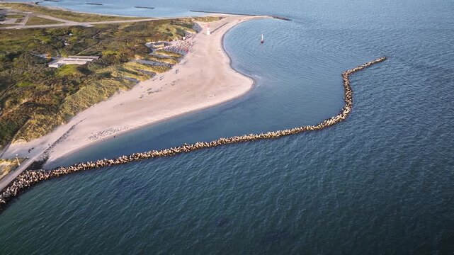 Aerial footage of D&uuml;ne, sandy sister island of Helgoland, Germany with wide beach, rolling dunes, beach chairs and red-white lighthouse, while long curved rock breakwater shelters bay on North Sea. 