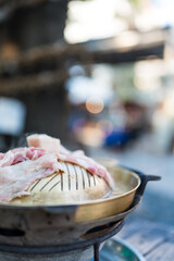 A Thai barbecue grill with fresh pork slices cooking on a hot pan. Authentic Asian street food style.