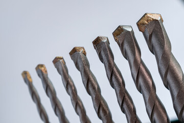 Alignment of seven tungsten carbide-tipped masonry drill bits against a white background: Represents construction tools, hardware, engineering, and DIY repair projects