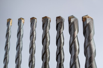 Alignment of seven tungsten carbide-tipped masonry drill bits against a white background: Represents construction tools, hardware, engineering, and DIY repair projects