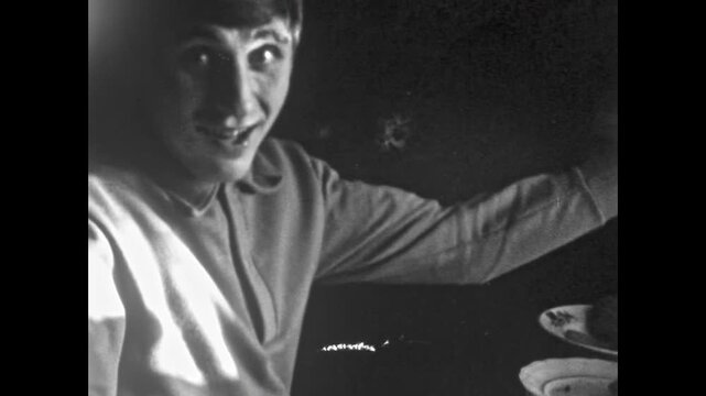 Vintage film, Happy man eating meal sitting at table, looking at camera, talking with his mouth full. Humor conversation with food. Everyday life. Black white old archive. Archival retro 1960s