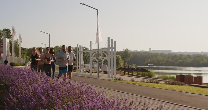 Concentrated team of runners jogging together outdoors in city park, engaging in group sport workout, boosting running effort, uniting in fitness and run training, enhancing jog performance.