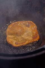 Golden flatbread or dough puffing up as it deep-fries in bubbling hot oil within a dark pan, showcasing rustic and traditional cooking methods. 