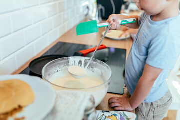 Close-up of child hands ladling pancake batter in home kitchen