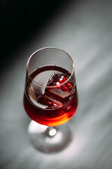 Rich ruby-red cocktail served in a contemporary stemmed glass, accented by a square ice cube with a frozen red berry inside. Luxury bar setting.